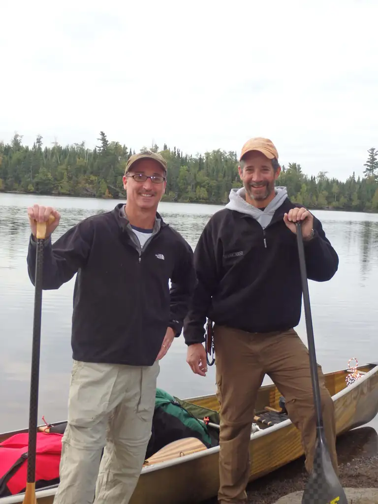 two men with paddles in front of canoe and poplar lake